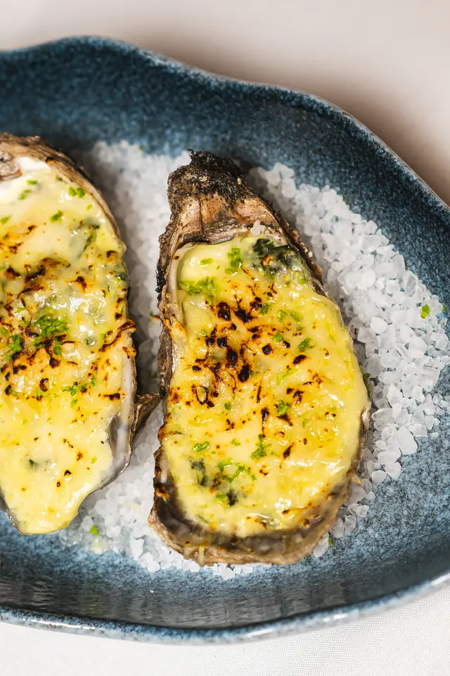 Broiled Rockefeller oysters with golden melted cheese over rock salt on a blue plate