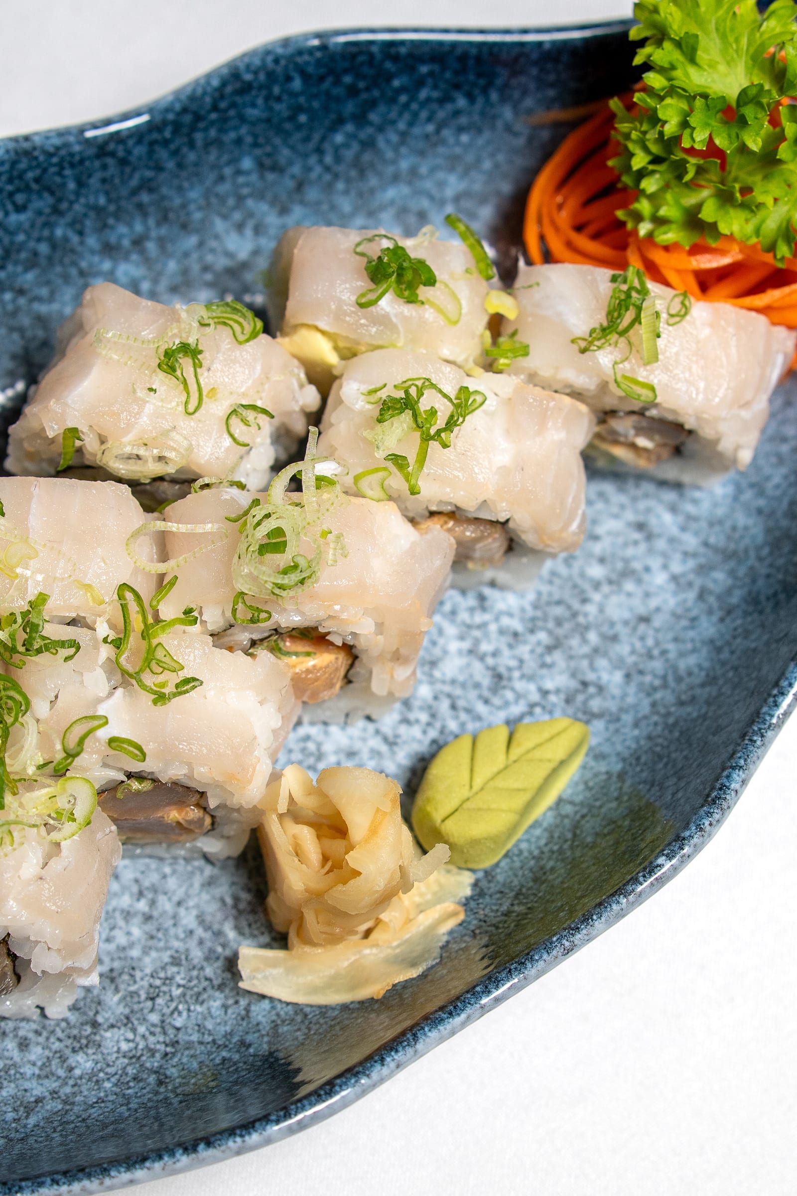 Close-up de rollo de sushi cubierto de pescado blanco fresco con cebollín, jengibre encurtido y wasabi en Cancún Centro