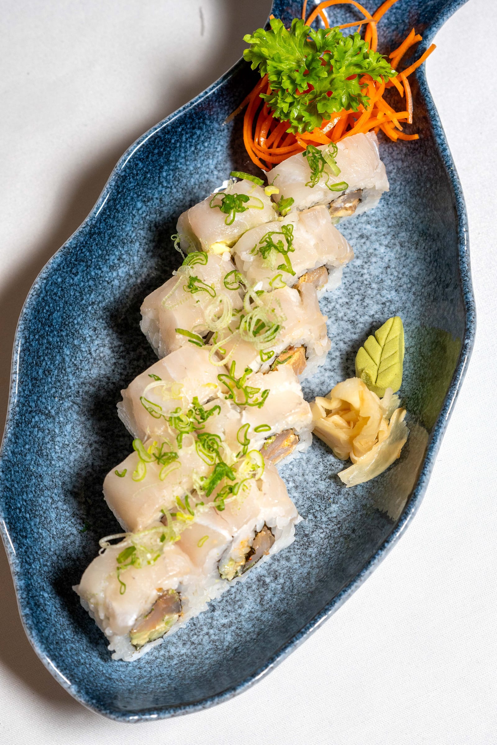 Rollo de sushi fresco de pescado blanco visto desde arriba en plato azul con forma de hoja, en MERO 18, Cancún Centro