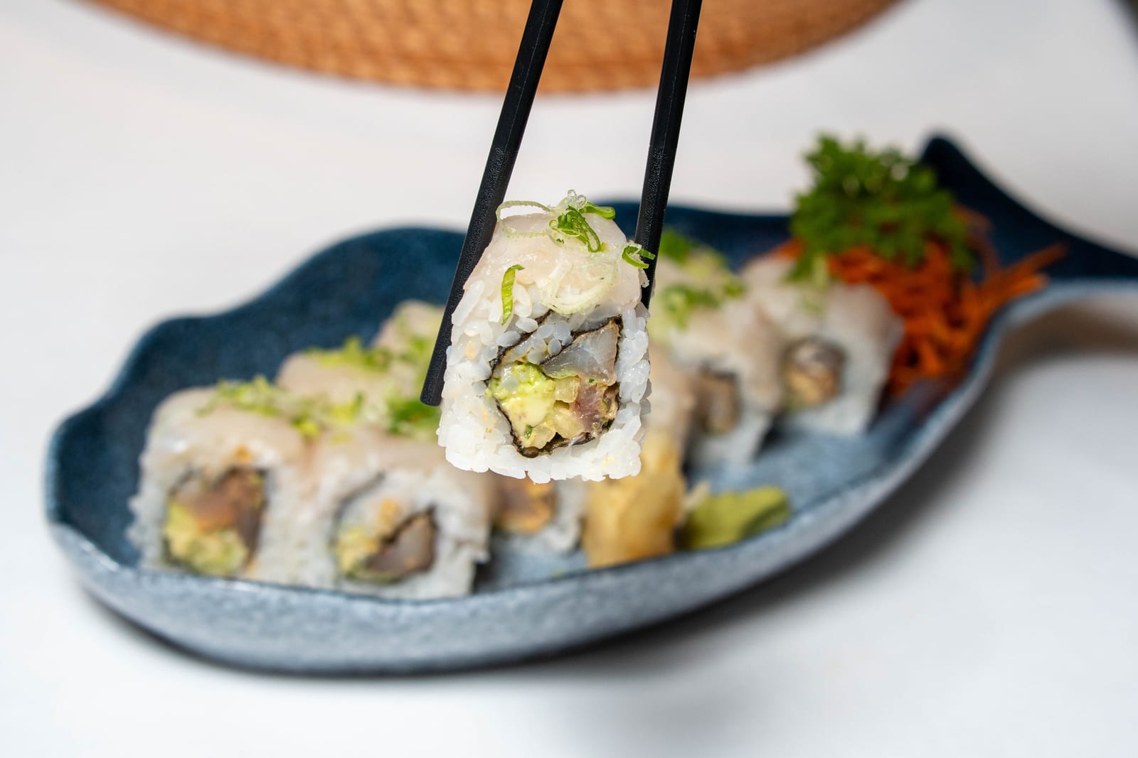 Pieza de sushi fresco con aguacate y pescado sostenida con palillos sobre plato azul en un restaurante del centro de Cancún