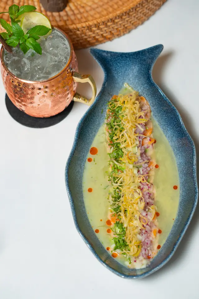 Salmon tiradito in leche de tigre with cilantro and crispy leek on a blue plate