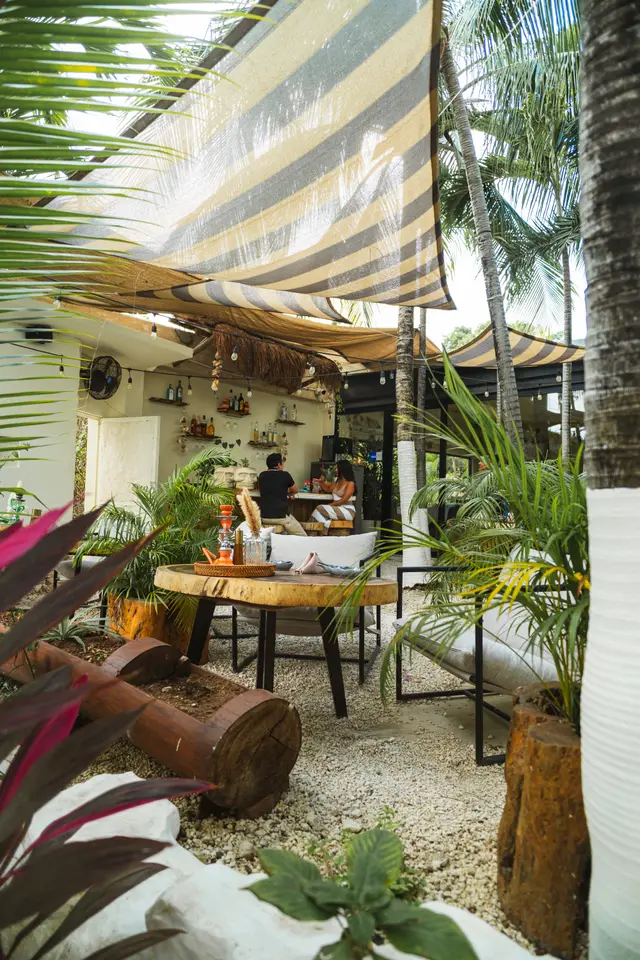 MERO 18's patio lounge with striped shade sails, palms and live-edge wood tables