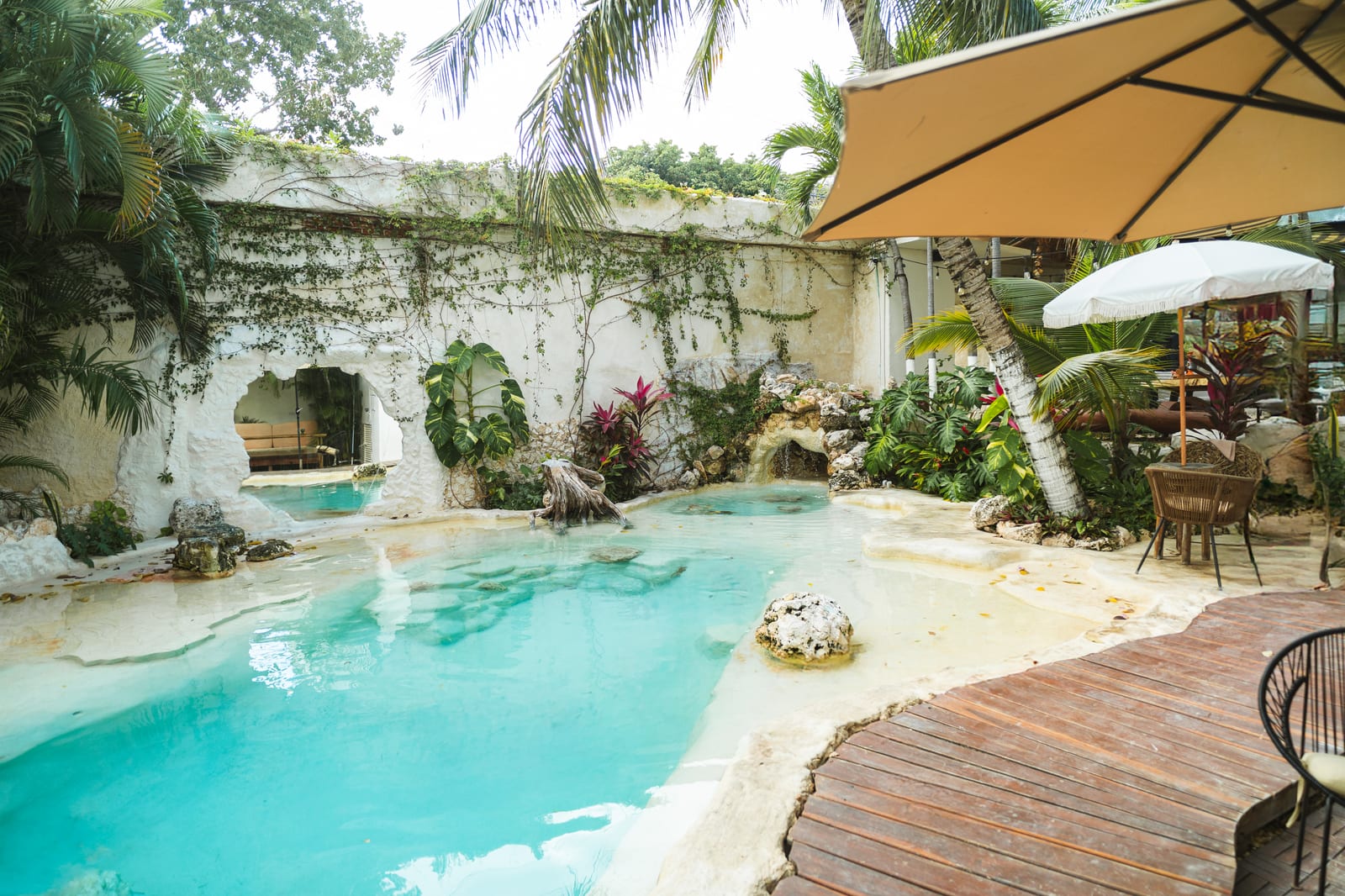 Alberca tipo cenote con cascada, muros cubiertos de enredaderas y palmeras en Mezcal Boutique Hotel