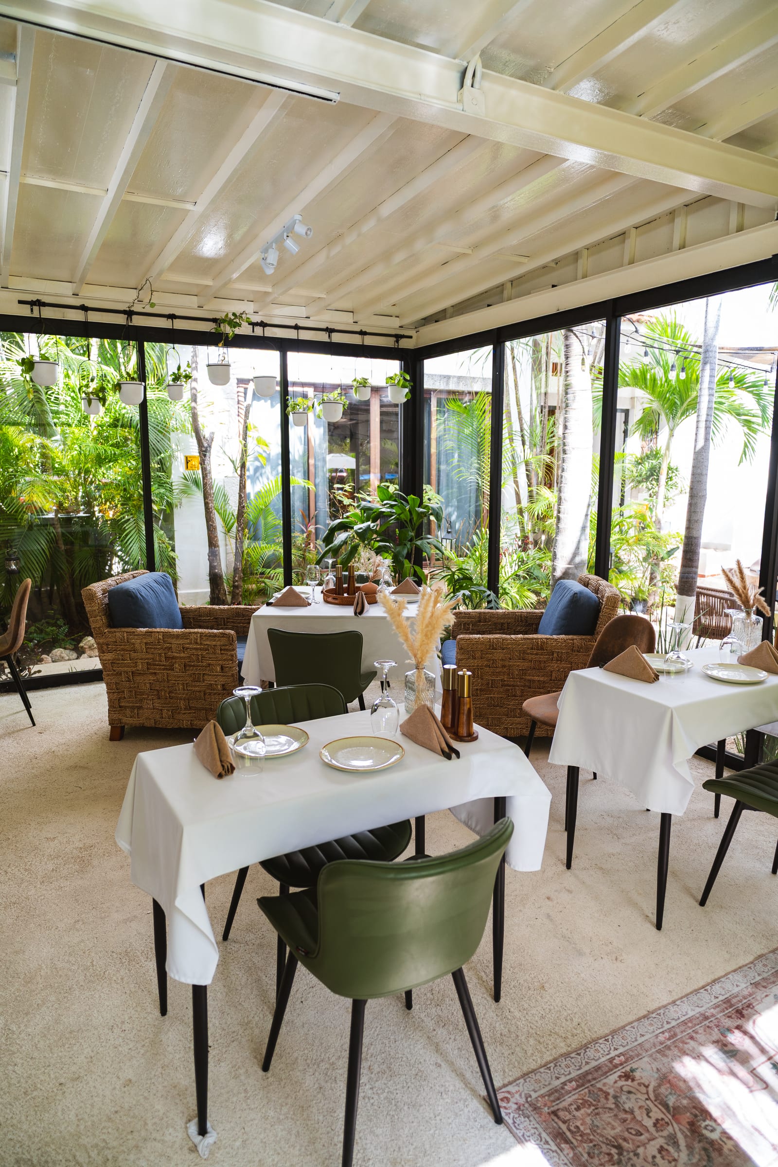 Glass-walled dining room at MERO 18 with rattan armchairs and a view of the tropical garden in downtown Cancún
