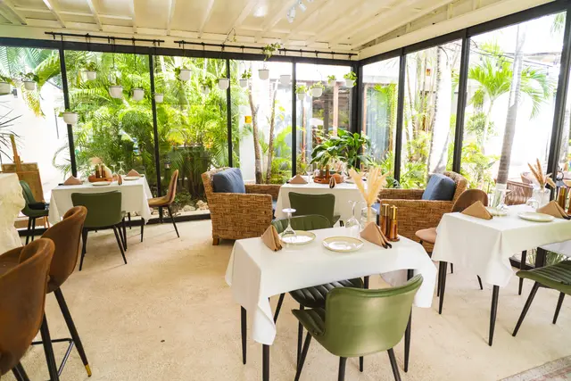 Glass conservatory dining room with white-dressed tables and pampas centerpieces facing the garden