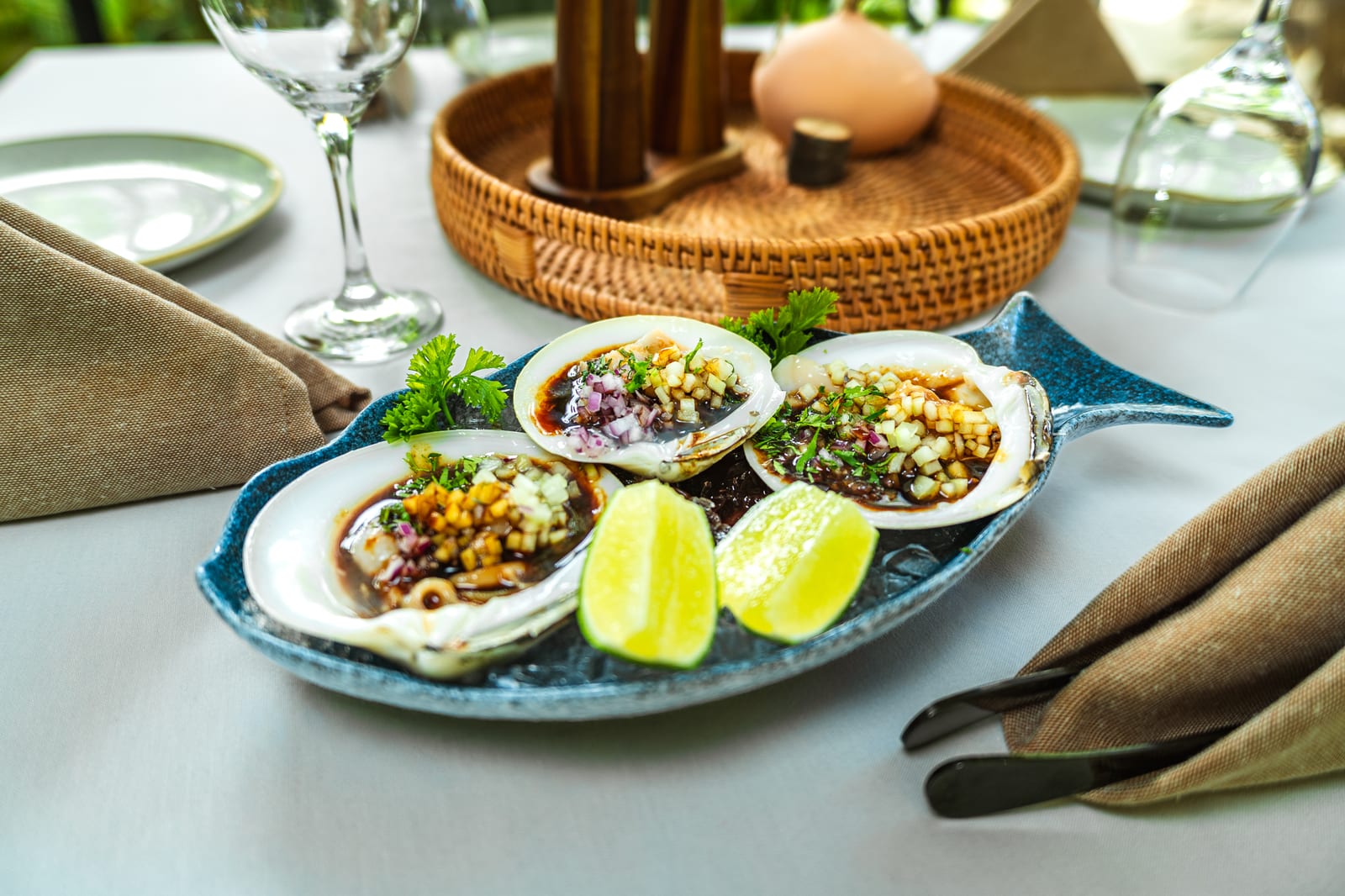 Almejas frescas servidas en su concha con salsa oscura, cebolla morada, pepino picado y limón en la barra fría de MERO 18, Cancún