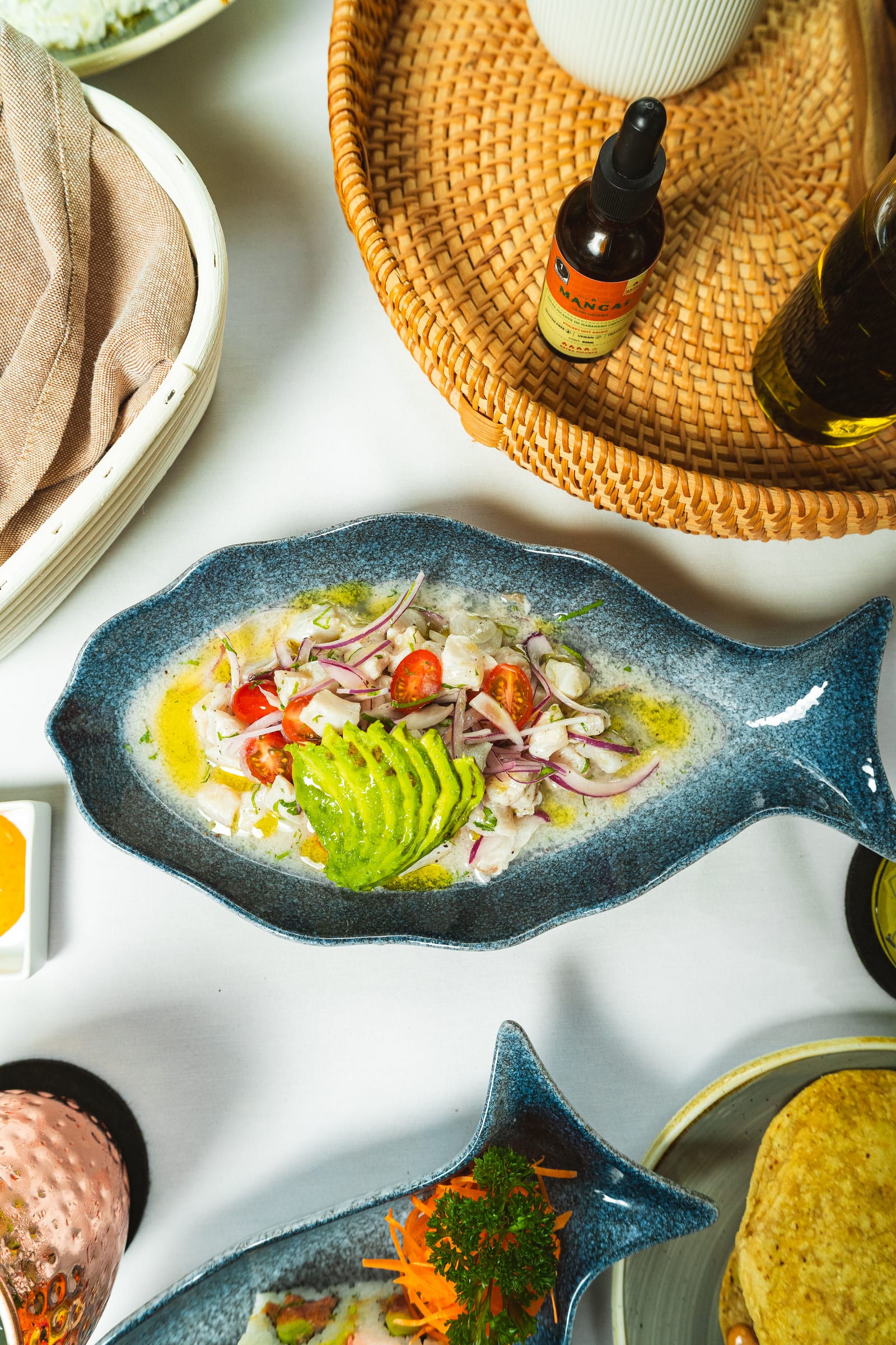 Ceviche de pesca del día en MERO 18: pescado fresco con abanico de aguacate, cebolla morada y jitomate cherry en plato azul con forma de pez
