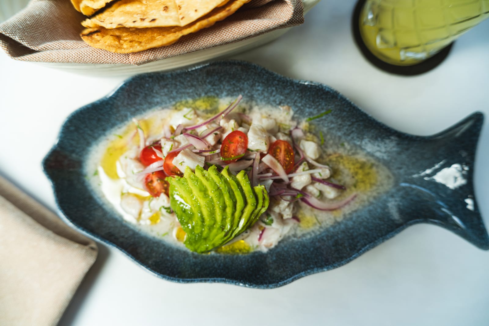 Ceviche de pesca del día con abanico de aguacate en plato azul con forma de pez, servido con tostadas de maíz en MERO 18, Centro de Cancún