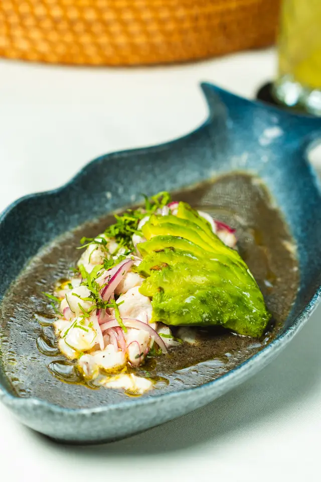Black aguachile with fresh fish, fanned avocado and red onion on a fish-shaped plate