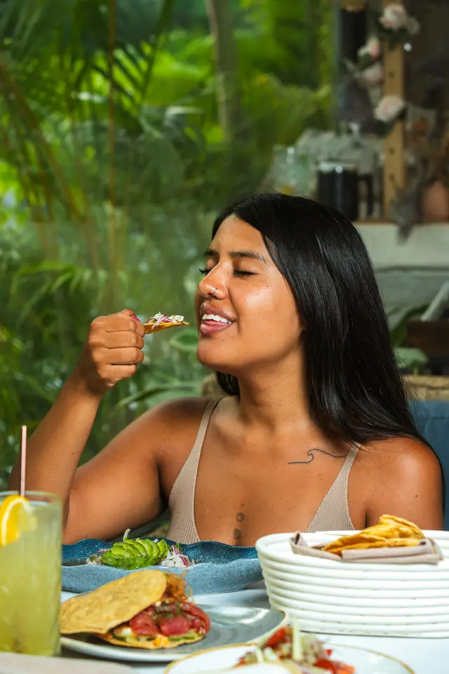 Guest savoring a ceviche tostada with her eyes closed amid the patio's jungle foliage