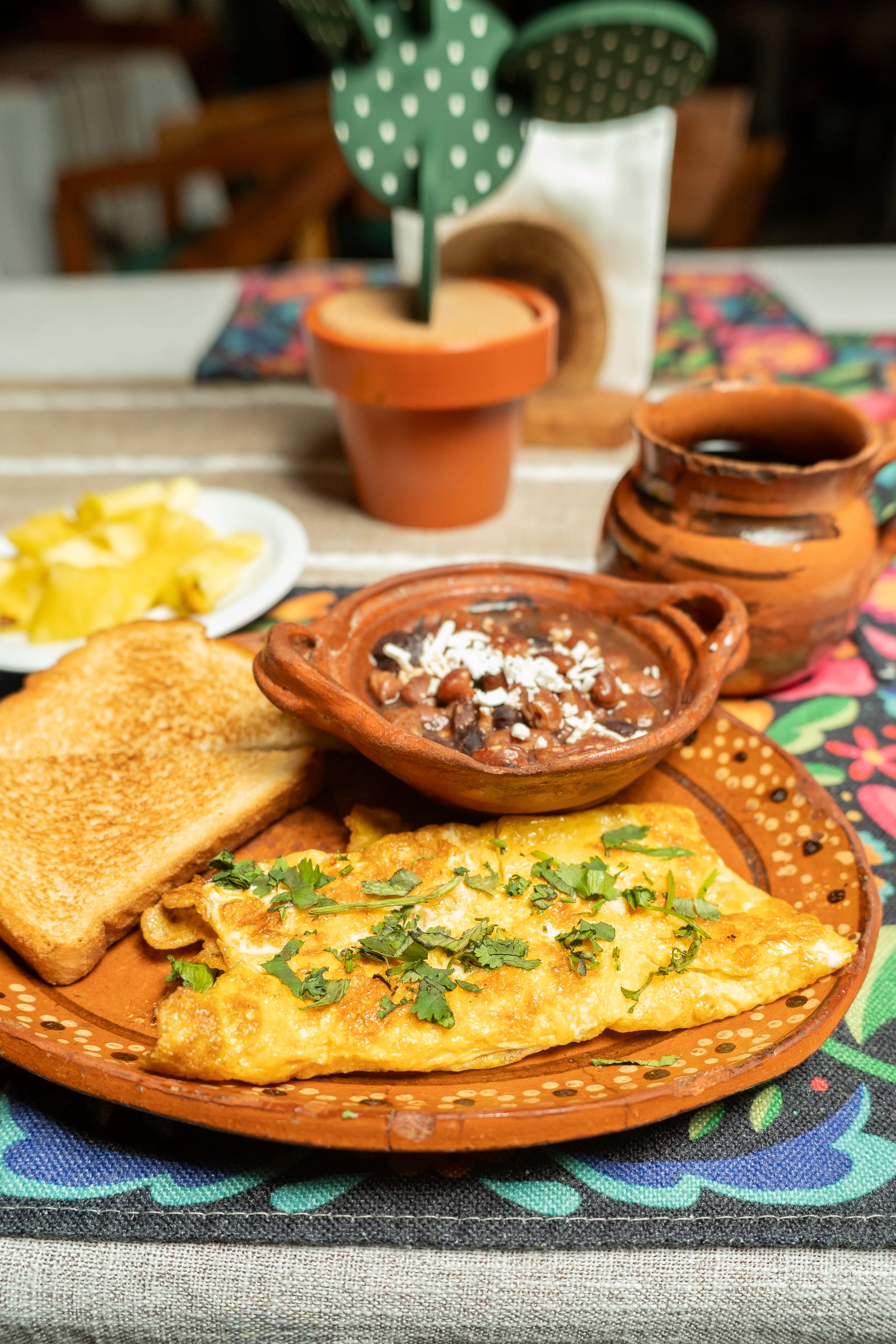 Omelette con cilantro en plato de barro, frijoles con queso, pan tostado y café servidos para desayunar en MERO 18