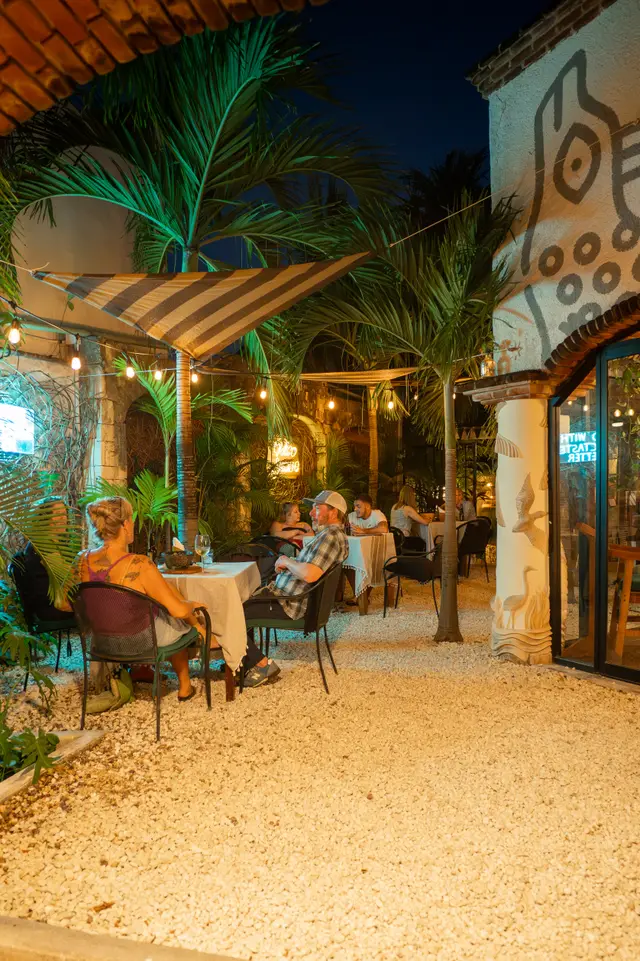 MERO 18's jungle patio at night, with diners under palms, shade sails and string lights