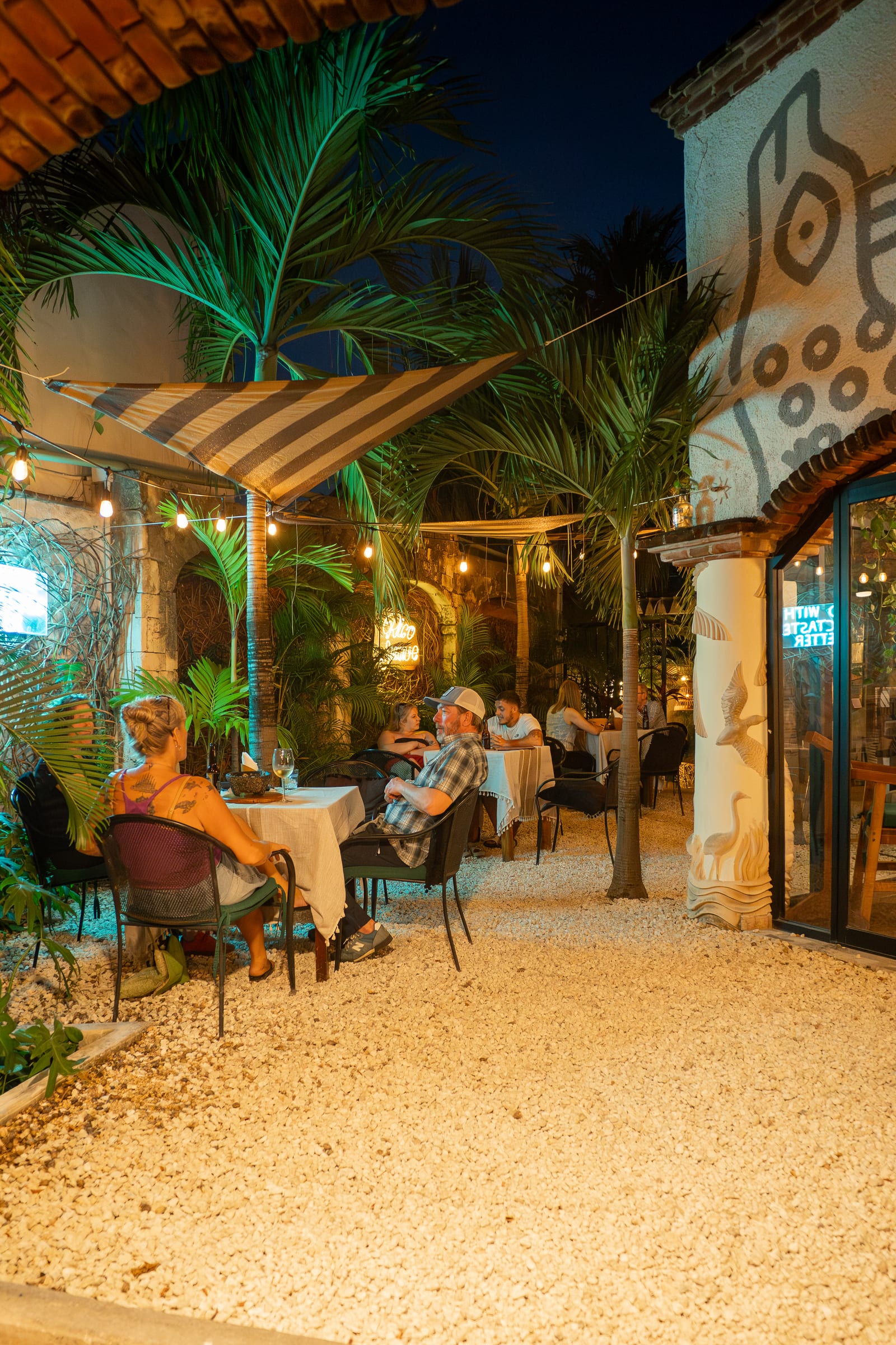 MERO 18's night patio with white-linen tables under palm trees and string lights