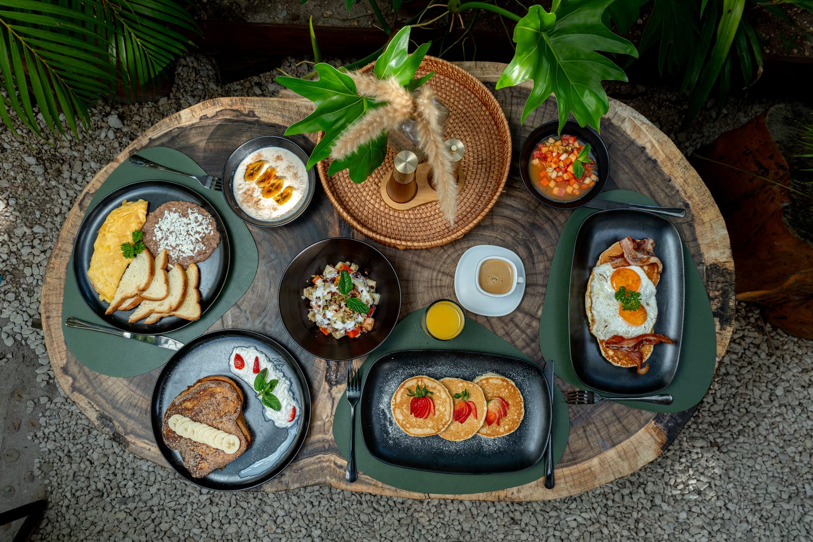 Overhead view of a brunch table at MERO 18 in Cancun with pancakes and strawberries, French toast, an omelette, eggs with bacon and juices