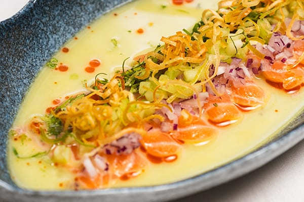 Primer plano de tiradito de salmón en leche de tigre con cebolla morada, apio y poro frito crujiente